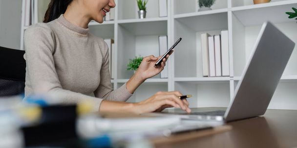 Geschäftsfrau nutzt Smartphone bei der Arbeit am Laptop, synchronisiert Daten zwischen Computer und Gerät im Büro, nutzt Firmengeräte und Geschäftsanwendung. - Foto, Bild