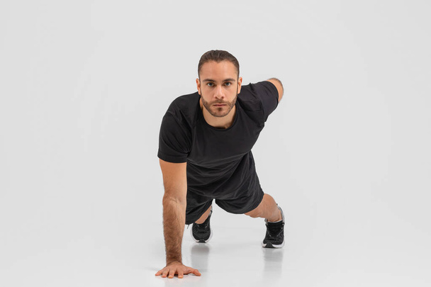 Determined young man in black athletic wear poised in a running start position against a white backdrop - Photo, Image