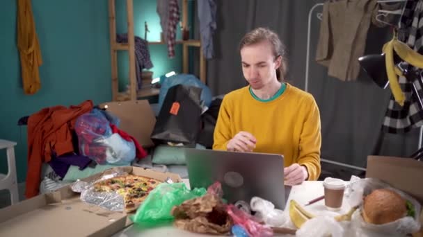 Diák vagy szabadúszó dolgozik otthon egy rendetlenség, tinédzser eszik pizza szállítás között kupac szemét és szétszórt dolgokat. Fénymásolási hely - Felvétel, videó