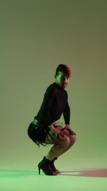 Energetikus és elegáns férfi magas sarkúban és bőrszoknyában, kortárs vagy divatos táncbemutatóval, zöld háttérrel. Függőleges videó. - Felvétel, videó