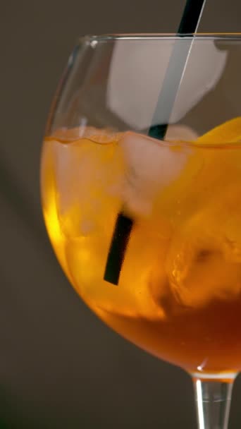 Glass of Aperol Spritz cocktail on gray background. Mixing Aperol Spritz with a cocktail straw. Vertical video - Footage, Video