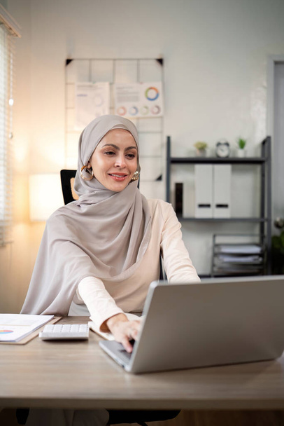 Donna d'affari musulmana asiatica in sciarpa hijab che lavora con documenti cartacei nell'ufficio moderno. diversità e concetto di ufficio. - Foto, immagini