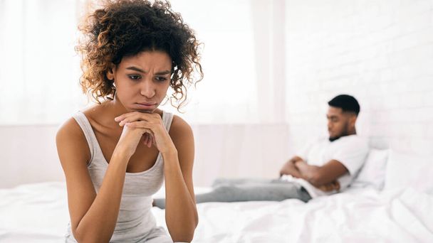 Thoughtful couple after quarrel lost in thoughts. Frustrated black girlfriend sitting on bed, thinking about relationship problems, empty space - Photo, Image
