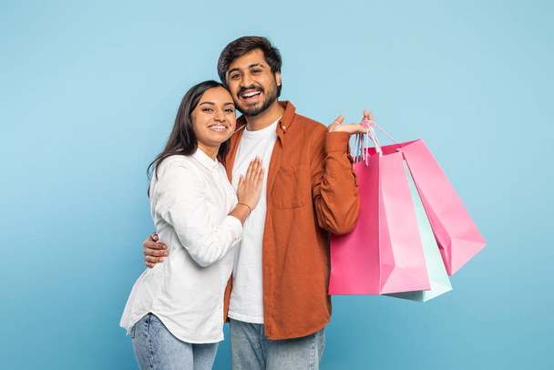 Affettuosa coppia indiana che tiene borse della spesa e abbraccia calorosamente, esprimendo vicinanza dopo lo shopping - Foto, immagini