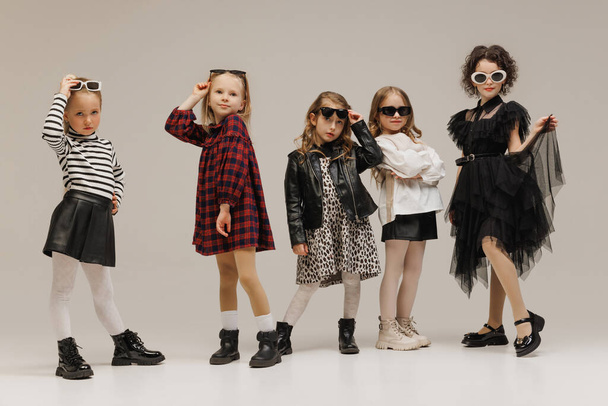 Cool little girls, elementary students posing wearing glamour outfits against grey studio background. Concept of childhood, kids fashion and beauty, style, school shopping. Black Friday - Photo, Image