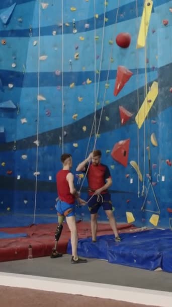 Verticaal breed schot van instructeur onderwijs man met onderste ledematen prothetisch hoe klimmateriaal te gebruiken in de sportschool - Video
