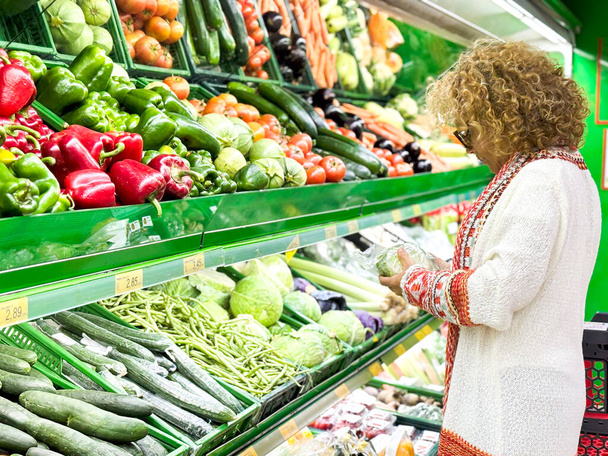 Gros plan portrait, belle, jolie femme en pull ramassant, choisissant des légumes verts à feuilles dans l'épicerie - Photo, image