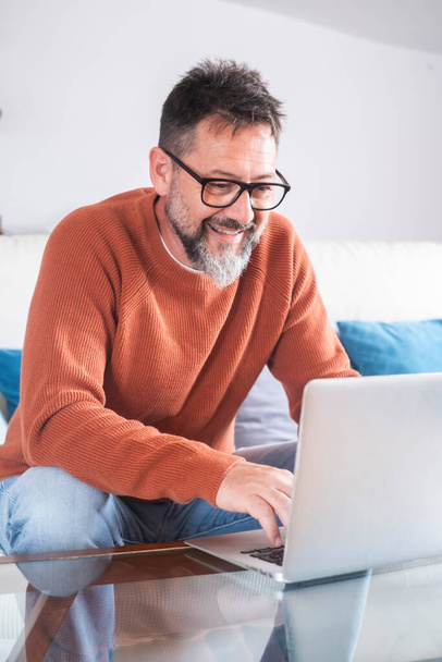 Hymyilevä vanhempi 50s mies istua rentoutua sohvalla olohuoneessa selaamassa internetiä moderni tietokone gadget, onnellinen kypsä freelance työntekijä levätä sohvalla kotona katsella video surffata langattoman verkon. Etsitään verkkoa - Valokuva, kuva