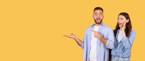 Man and woman in casual clothes acting surprised and pointing to empty space on yellow background - Photo, Image