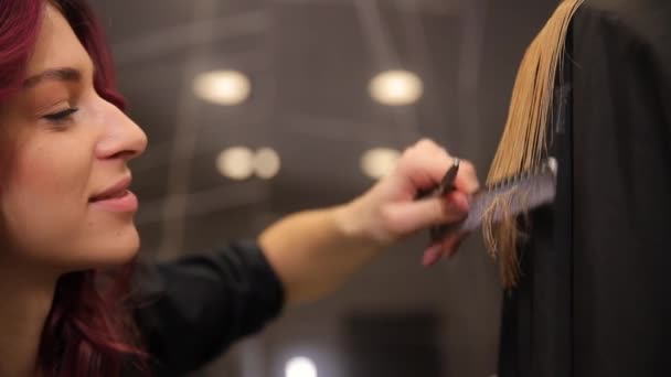 Primer plano de un corte de pelo de una larga rubia de pelo femenino. Un peluquero joven corta el cabello con la ayuda de herramientas de peluquería. - Imágenes, Vídeo
