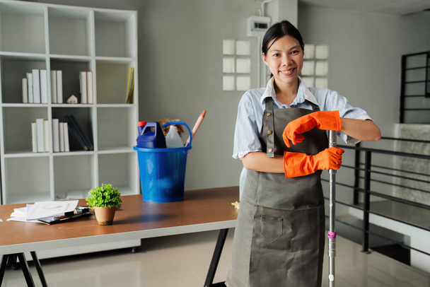 Sprzątaczka uśmiecha się i nosi rękawiczki, przygotowując się do sprzątania biura. - Zdjęcie, obraz