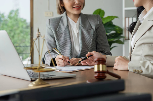 Une femme signe un document sur un bureau avec un ordinateur portable et une chaise. La femme porte un costume et écrit avec un stylo. La scène suggère un cadre professionnel - Photo, image