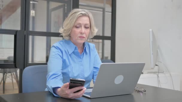 Idős nő dolgozik a telefon és a laptop - Felvétel, videó