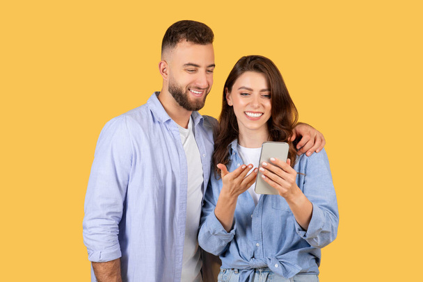 Счастливые мужчина и женщина смотрят на мобильный телефон вместе с желтым фоном - Фото, изображение