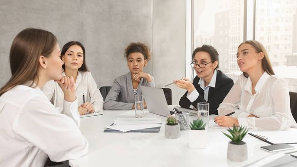 Eine Gruppe von fünf professionellen Frauen diskutiert an einem Konferenztisch in einem gut beleuchteten Büro - Foto, Bild