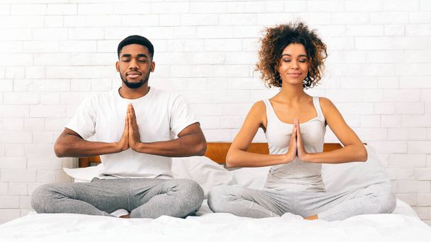 Barışçıl Afro-Amerikan çifti evlerindeki yataklarında meditasyon yaparken... - Fotoğraf, Görsel