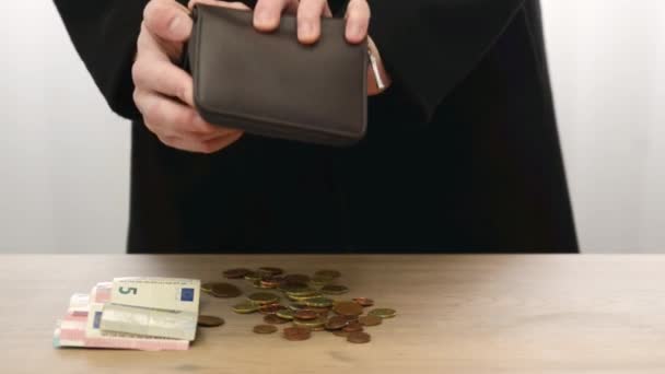Мужчина вытряхивает монеты евро и центы из бумажника рядом со смарт-банкнотами, считает деньги на столе рукой. Учет и контроль средств - Кадры, видео