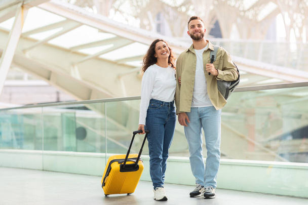 明るい黄色のスーツケースが歩いて旅行ターミナルで微笑んでいる楽しいカップル - 写真・画像