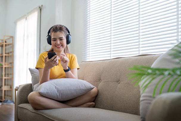 Fiatal ázsiai nő használ mobiltelefon és fülhallgató hallgatni zenét vagy online csevegés otthon. - Fotó, kép