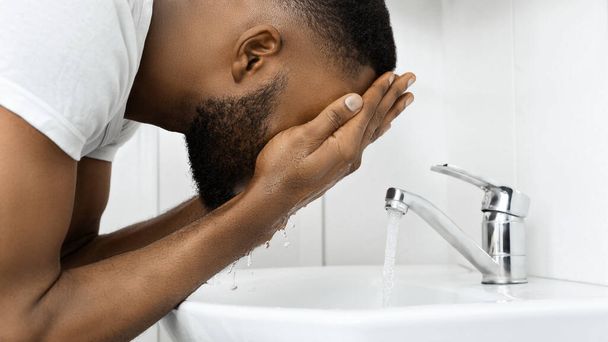 Αφροαμερικάνος με καθημερινή ρουτίνα να ρίχνει νερό στο πρόσωπό του για μια νέα αρχή της ημέρας. - Φωτογραφία, εικόνα