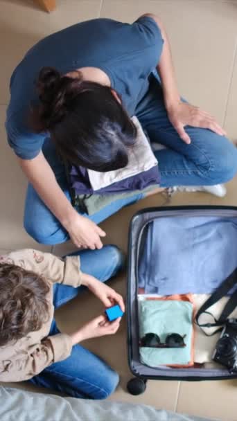 Вид сверху на вещи матери и сына в чемодане перед поездкой домой - Кадры, видео