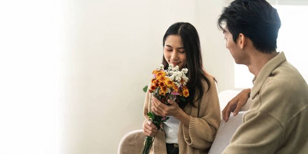 Asiatische gutaussehende Mann zeigen die Liebe und geben Blumen an seine Freundin im Wohnzimmer am Valentinstag. Lifestyle-Konzept. - Foto, Bild