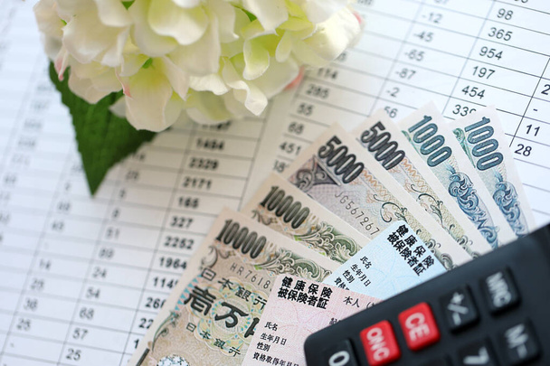 Carte sanitarie giapponesi azzurre e rosse sul tavolo con denaro giapponese in yen e calcolatrice da vicino - Foto, immagini