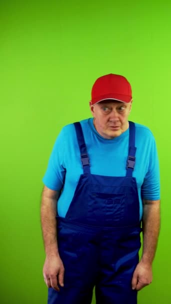 Repairman in overalls puts fingers to lips and says shhh demanding silence. Mature worker demanding shut up and waving his finger in negative. Green screen. Chroma key. Vertical. - Footage, Video