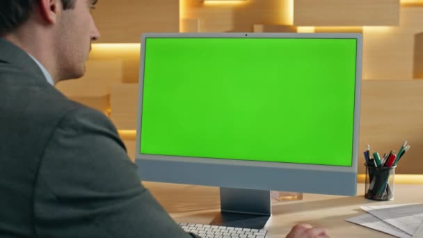 Johtaja, joka työskentelee kromakeyn tietokoneella ja katselee työpöydän lähikuvaa. Mies lukee sähköpostia vihreän ruudun tietokoneella modernissa asunnossa. Liikemies käyttää langattoman suun näköinen mockup monitori sisätiloissa - Materiaali, video