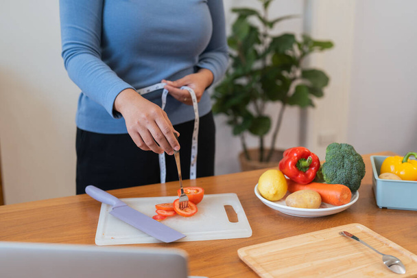 Młoda Azjatka mierzy talię w kuchni warzywami i owocami. Pojęcie zdrowego odżywiania i diety. - Zdjęcie, obraz