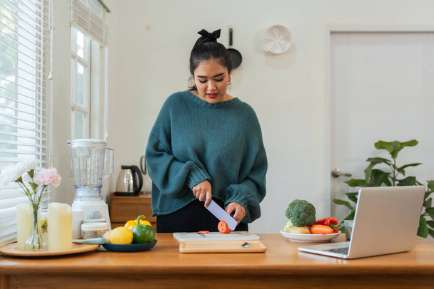Dicke Frauen kochen in der Küche und hacken frisches Gemüse auf dem Schneidebrett. Lernen Sie, Salate und gesunde Lebensmittel aus dem Internet zu machen. Gesundheitskonzept Gesunde Ernährung zum Abnehmen. - Foto, Bild