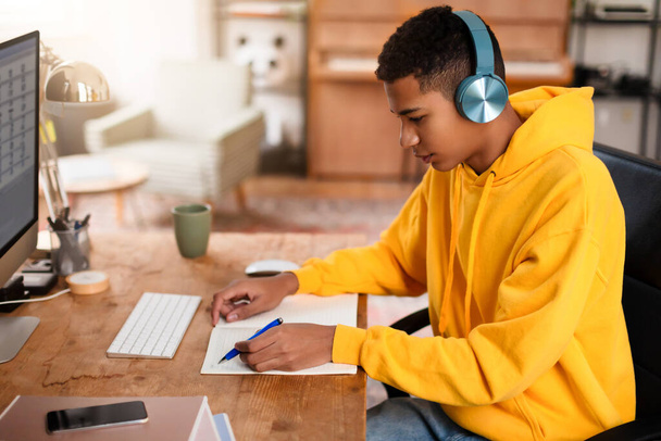 Людину бачать, як вона пише в блокноті за столом, з комп'ютером і навушниками поблизу - Фото, зображення