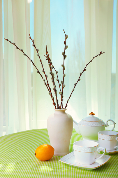 Willow twigs, teapot, cups and citrus on table on curtains background - Foto, Bild