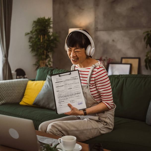 volwassen vrouw japans zakenvrouw hebben video oproep gebruik laptop werk van thuis online overleg of conferentie show papier document contract aanbod of stats - Foto, afbeelding