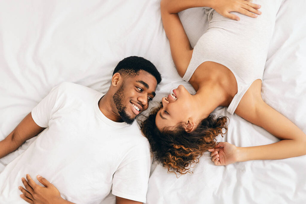 Bovenaanzicht van Afrikaans Amerikaans echtpaar dat zich bezighoudt met een tedere omhelzing op het bed, benadrukken genegenheid en comfort in relaties - Foto, afbeelding