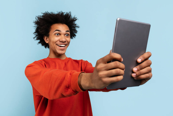 Egy boldog afro-amerikai férfi készít egy szelfit egy digitális tablettel, boldog csodálkozást fejezve ki. - Fotó, kép