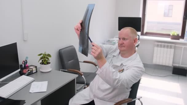 Ein Arzt analysiert ein Röntgenbild in einem gut ausgeleuchteten Büroumfeld. - Filmmaterial, Video