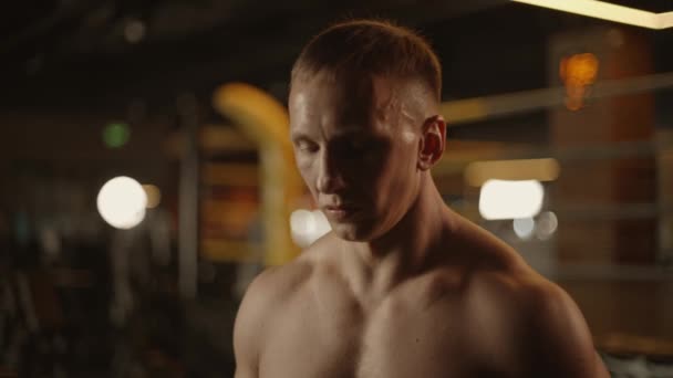 Portrait of young handsome tired and sweaty Caucasian man boxer looking at camera with serious look at dark gym hall. Close up of sporty male fighter after exercising in cross training workout space.  - Footage, Video