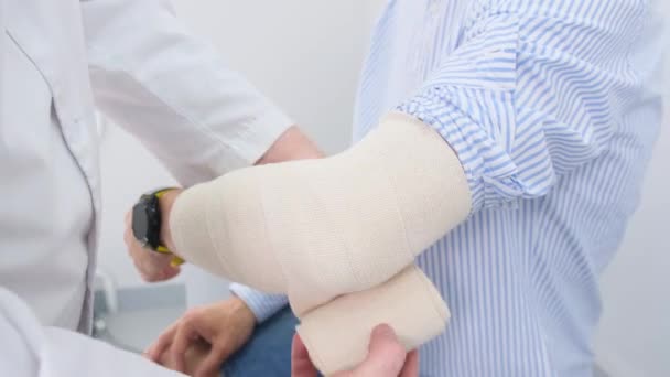 Een arts beveiligt een verband rond een gewonde arm van een patiënt.. - Video