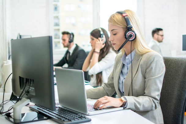 Krásná mladá pracovnice zákaznické podpory se sluchátky pracující na notebooku v call centru - Fotografie, Obrázek