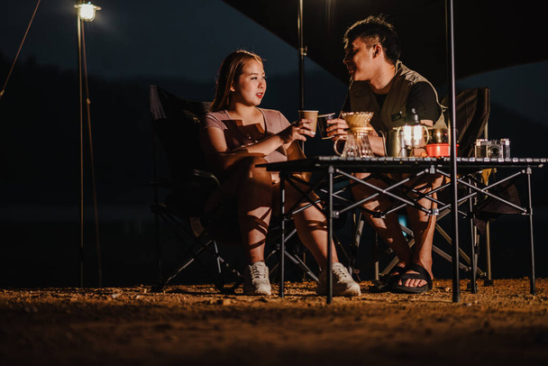 Çiftler, çevre aydınlatması altında huzurlu kamp alanlarında sıcak bir içki içip sohbet ediyorlar.. - Fotoğraf, Görsel