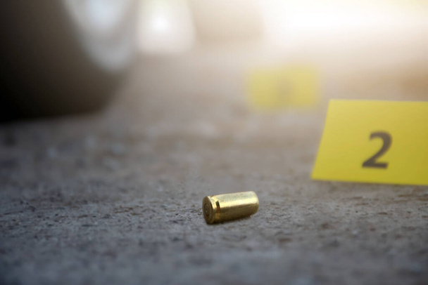 Pistolenkugelhülse auf Zementboden mit verschwommenem gelben Papier und Zigarettenfilterresten Hintergrund, Konzept für Ermittlungen und Verbrechen durch Polizeibeamte und Investoren, weicher Fokus. - Foto, Bild