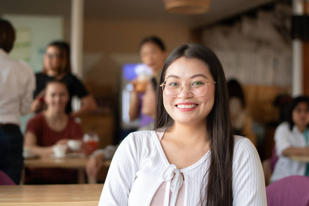 Asian young adult woman in white t-shirt holding woven fabric which was decorated on ceiling of local cafe for tourist watching and taking photos, soft focus, happiness of humans concept. - Photo, Image