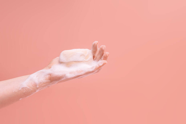 Mani insaponate femminili che tengono un pezzo di sapone su uno sfondo rosa. - Foto, immagini