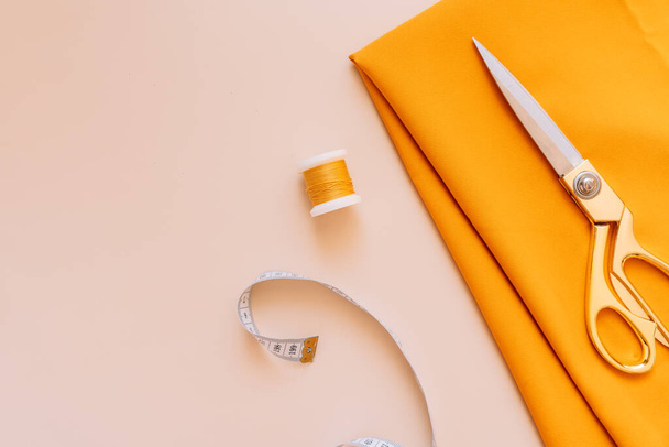 Швейна ножиці лежать на помаранчевій тканині поруч з нитками і мірною стрічкою. - Фото, зображення