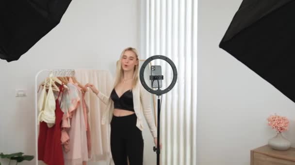 Genç sosyal medyum kadın moda videosu yapıyor. Blogcu kameraya ve ışık çemberine gülümserken, aynı zamanda ikna edici çevrimiçi kıyafetleri izleyicilere veya takipçilere vlog sattırıyor. Blithe - Video, Çekim