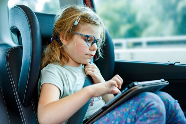 Маленька дівчинка грає планшет всередині машини. Сім'я їде у відпустку. Дошкільна дитина розважається - Фото, зображення