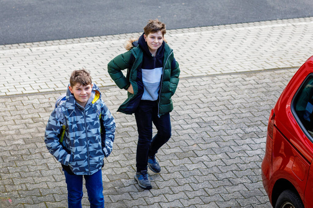 Two happy school students walking on street after school and chatting. Teenager boys, brothers and friends. Portrait of joyful young boys pupils with backpacks in good mood speaking outdoors in city - Photo, Image