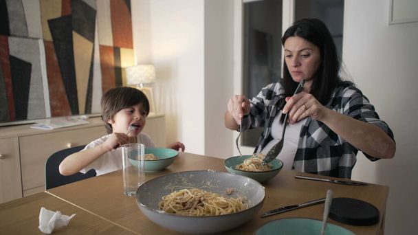 Illallinen yhdessä - Äiti tarjoilee spagettia Pasta lautasella, kun poika syö ruokaa, hoivaaminen Ateriaaika Bond kotona - Valokuva, kuva