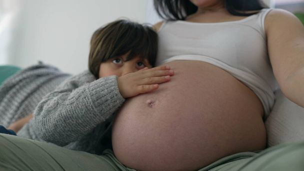 Lapsi varovasti hieroo äidin raskaana olevaa vatsaa raskauden kolmannen kolmanneksen aikana, onnellinen sydäntä lämmittävä perhehetki, lähikuva kasvot ja käsi. - Valokuva, kuva